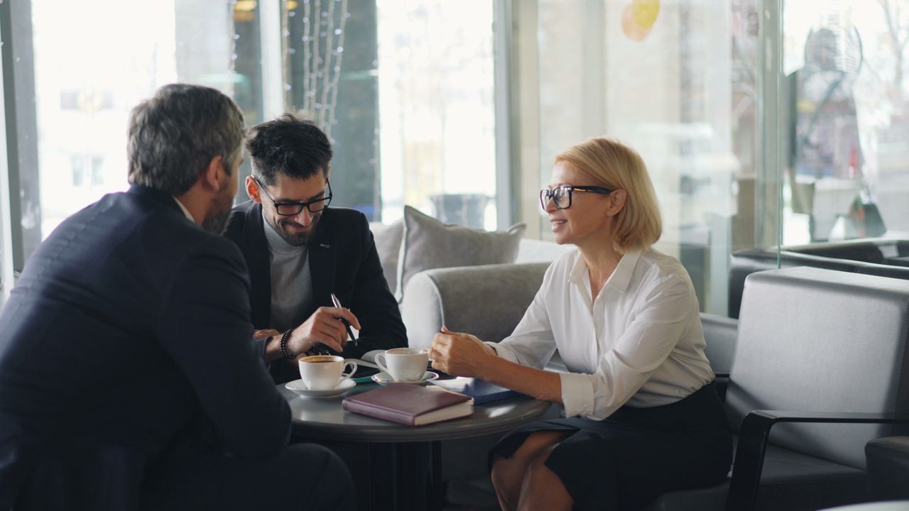 about-us Three professionals engaged in a business meeting at a cafe.